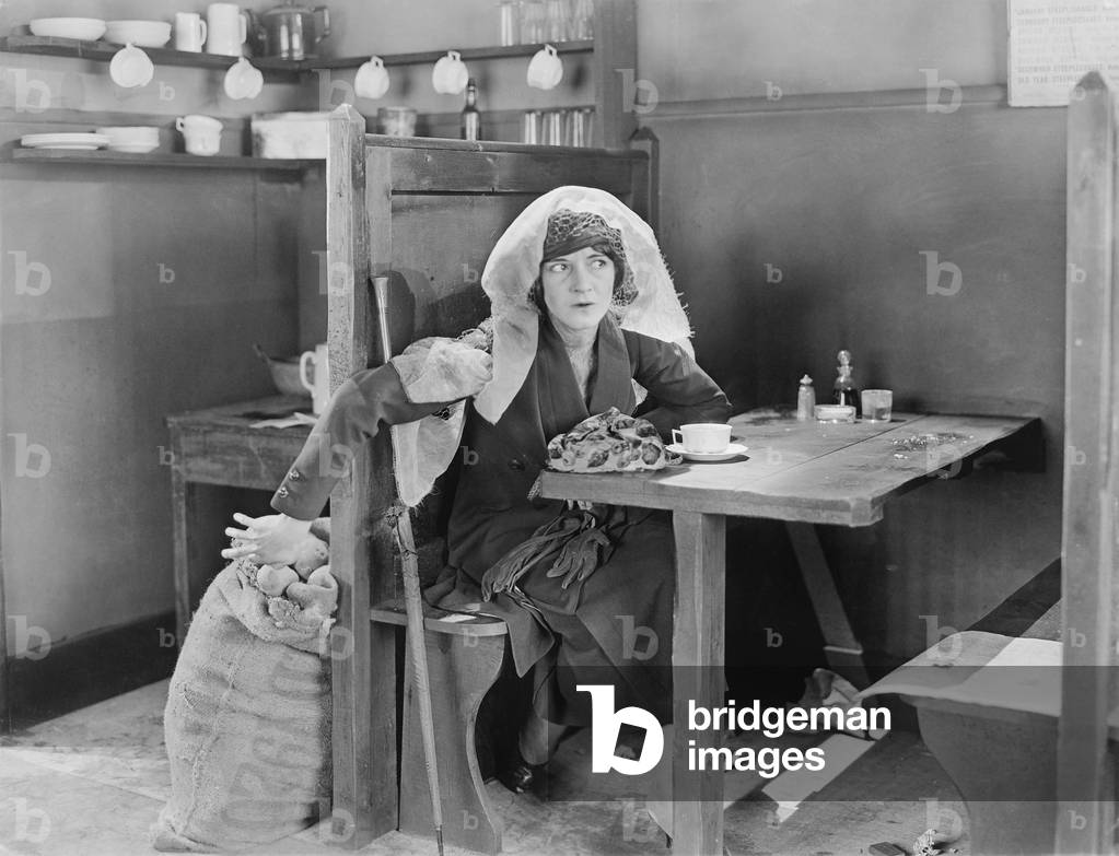 Young Woman Sitting in a Booth in a Diner, Trying to Steal Something Out of a Jute Bag