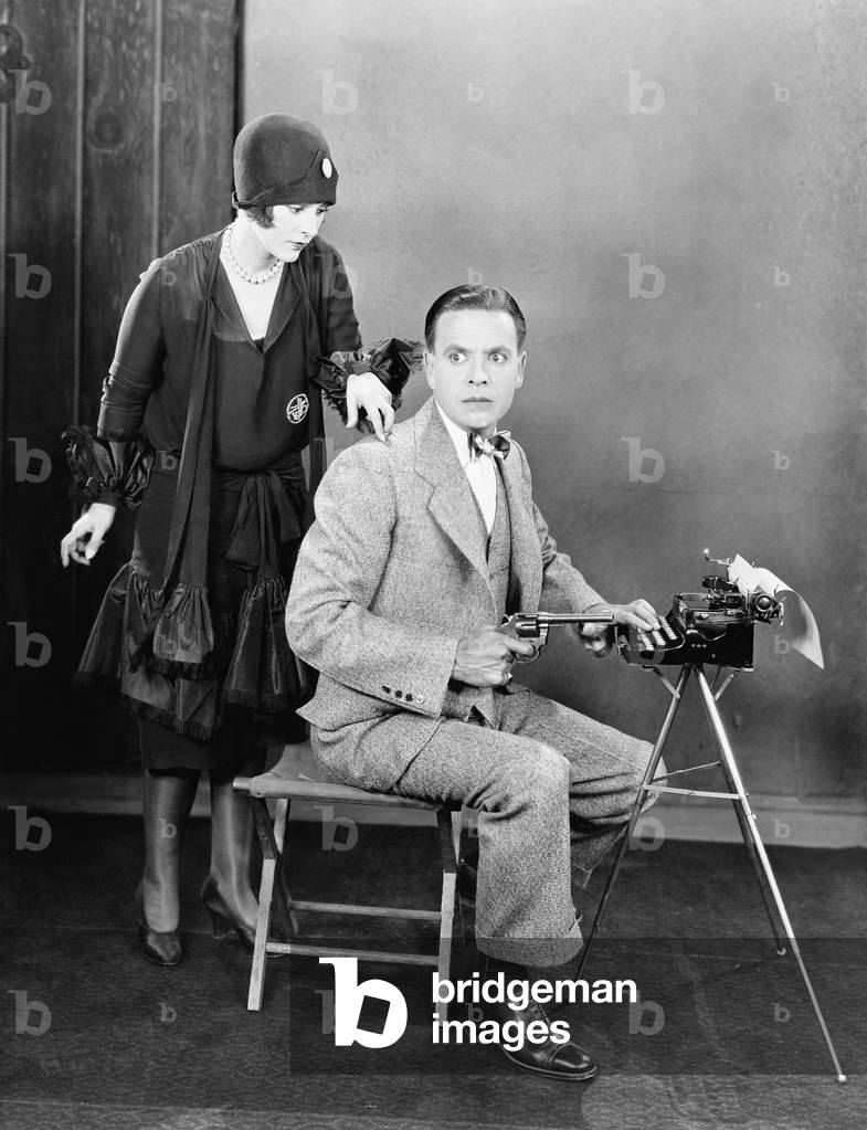 Man at a Typewriter Holding a Gun and a Woman Tapping on his Shoulder