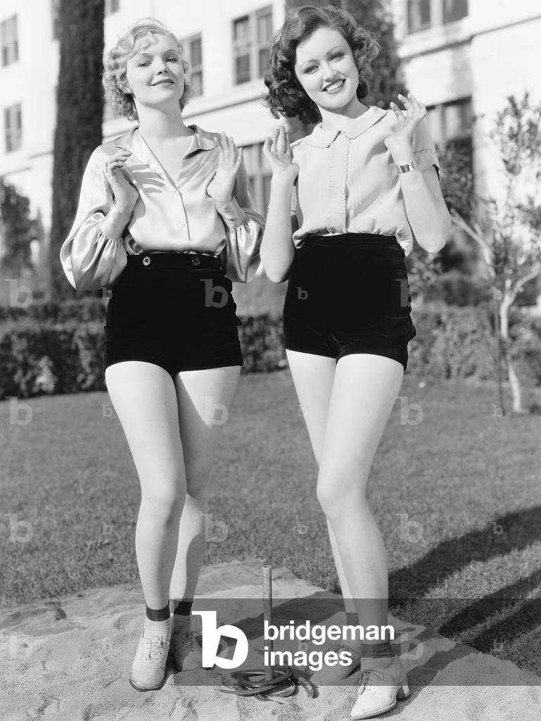 Two Young Women Standing Together Playing Horse Shoes