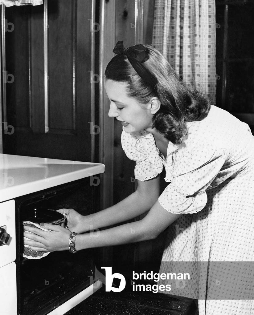 Young Woman in her Kitchen Pulling a Pot Out of the Oven