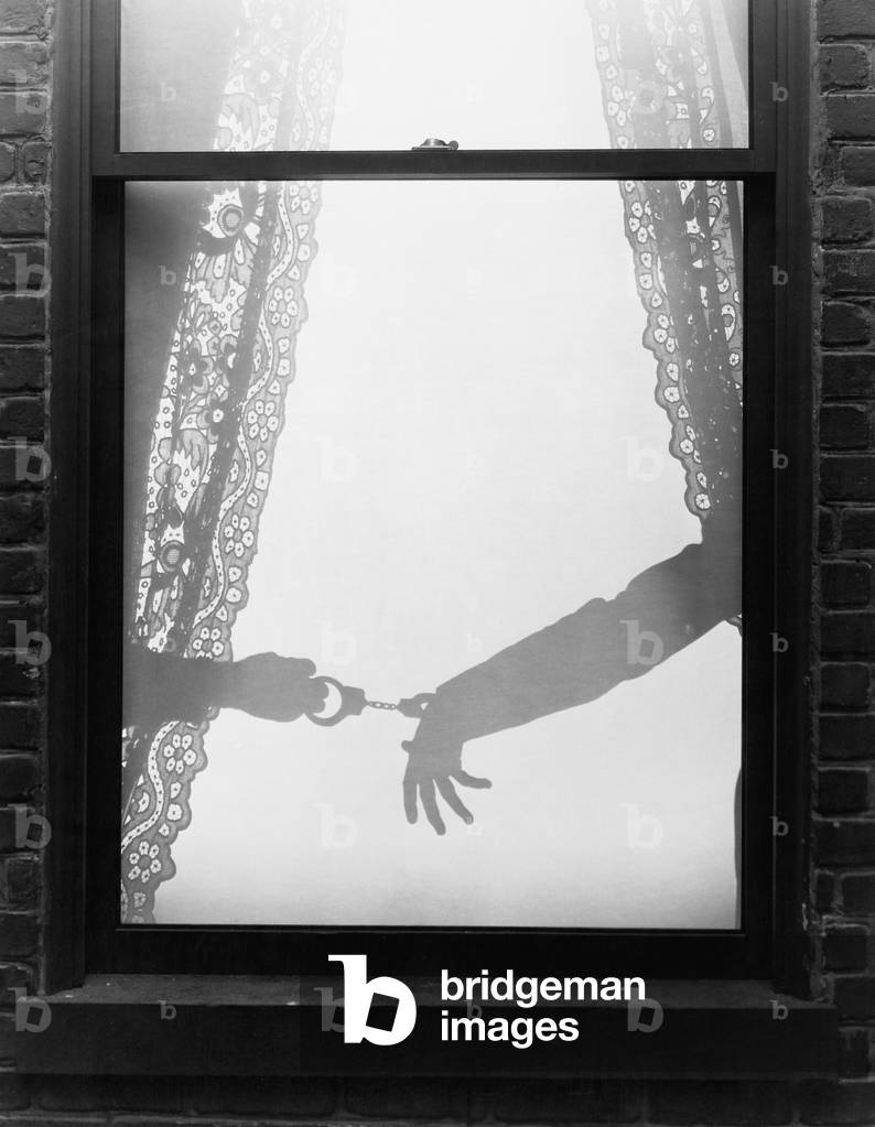 Silhouette of a Hand Arresting a Person with Handcuffs Viewed Through a Window 1910-40 (b/w photo)