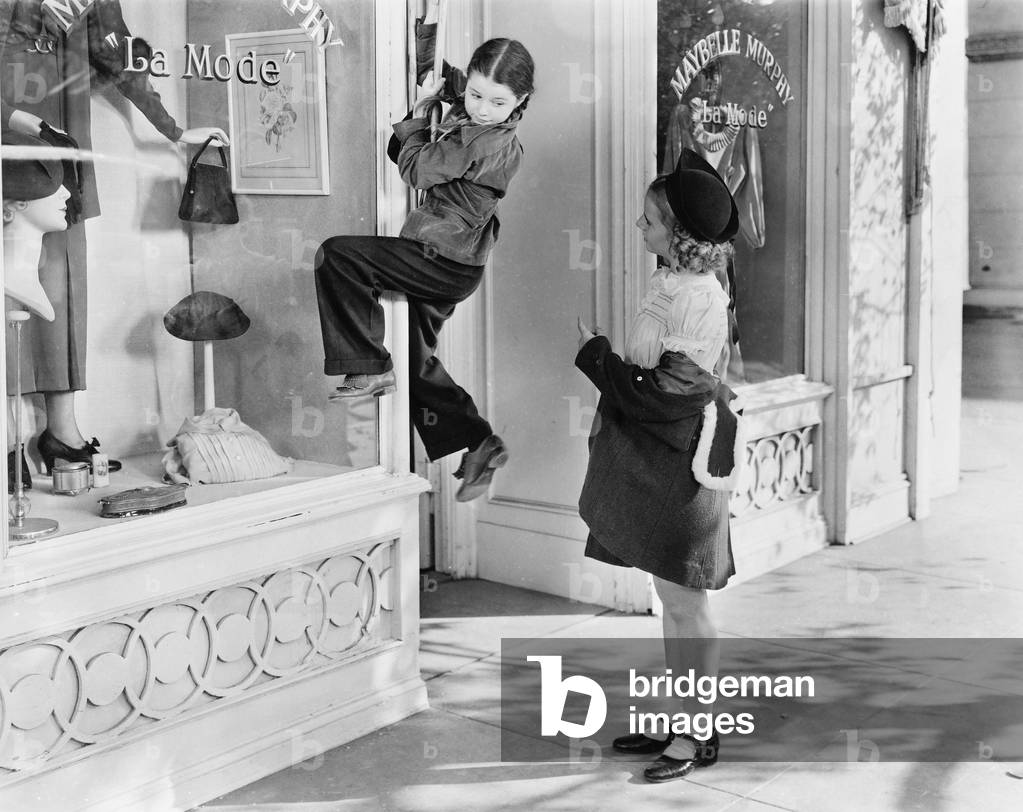 Two Girls on the Street with One Climbing on a Display Window