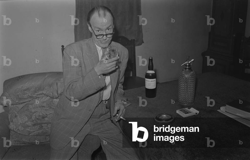 Comedy pose with a drink. Chuck O'Neil, a comedian, pictured at the home of Dr E.A. Stroud, College Street, Nuneaton. November 1954