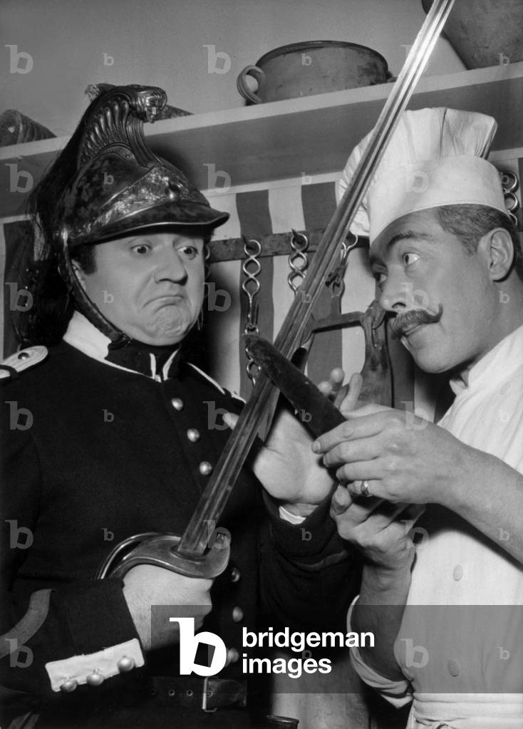 Jean Richard Comparing His Sabre To The Dragon Cook's Knife On Jeanrenoir's “Elena And Men” Film Set December 16, 1955 - Jean Richard (L) on Set of Film “Elena And Men” December 16, 1955 (b/w photo)