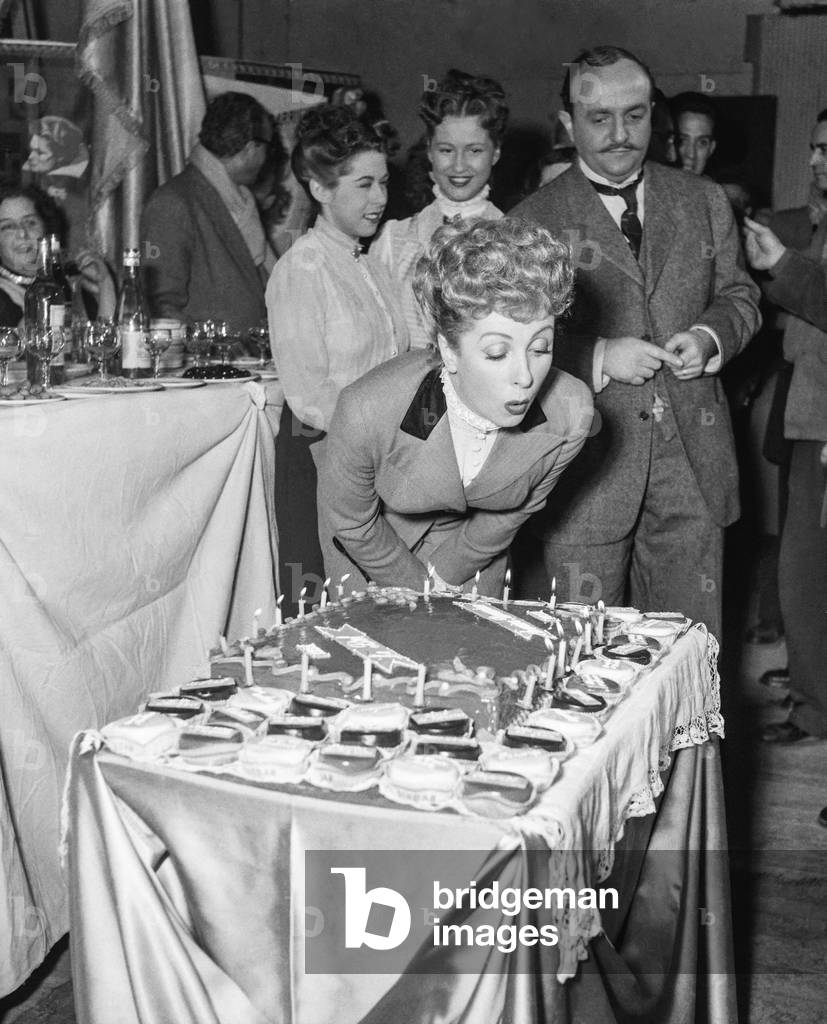 French actress Danielle Darrieux celebrating her 20-year career, at the Epinay studios, near Paris, March 30, 1951 : Danielle Darrieux blowing out the candles and in the background Bernard Blier (b/w photo)