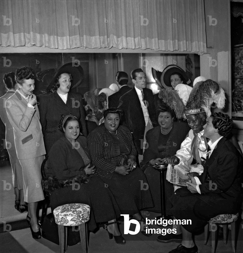 Party given at beauty institute of Lisette Pariente in Paris, June 10, 1949 : Colette Mars, Mathilde Casadesus, Mr et Mme Jean Farrel, les 3 Peters sisters, Ras Prince Monolulu (Peter Carl Mackay), Lisette Pariente (b/w photo)