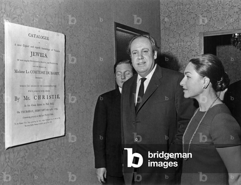 Christopher Soames And Princess Jeanne Marie De Broglie At The Paris Office Of Christie's In Front Of The Poster Announcing The Sale Of Jewellery Of Mrs. Dubarry November 5, 1968 (b/w photo)