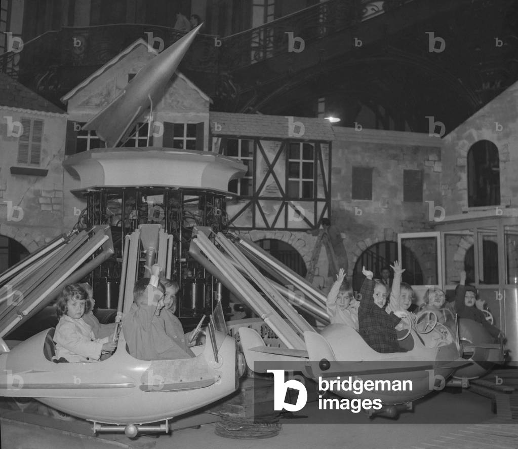 Preparations of the childhood fair at the Grand Palais in Paris on October 26, 1960 : here children on a mery-go-round (b/w photo)