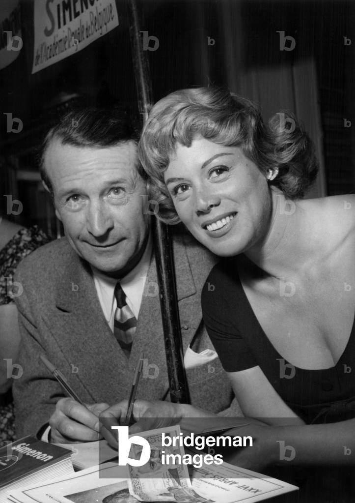 The French Writer George Simenon With The Actress Dora Doll at Book Fair in Paris, June 1, 1956 (b/w photo)