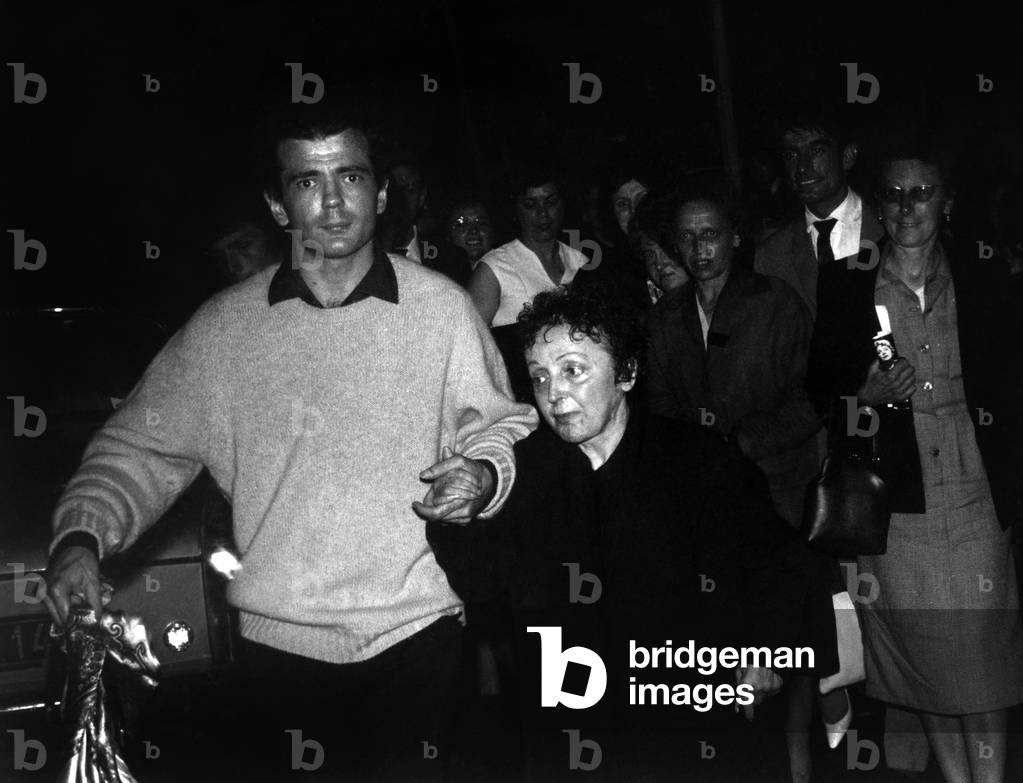 Edith Piaf, Very Escorted And Escorted By The Crowd After Her Singing Tour In Caen, Leaning On The Arm Of Her Secretary Claude Figus. June 21, 1962 (b/w photo)