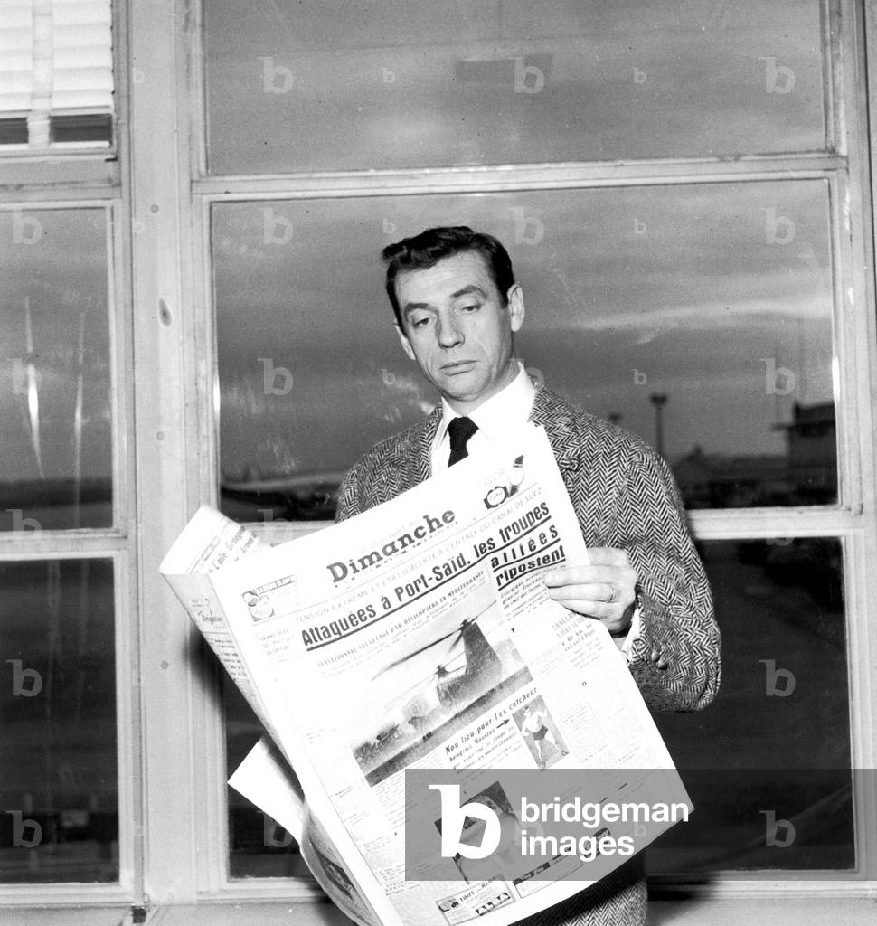 Yves Montand Reading Newspaper About Suez Crisis December 16, 1956 at Paris Orly Airport, Before Leaving For Moscow (b/w photo)
