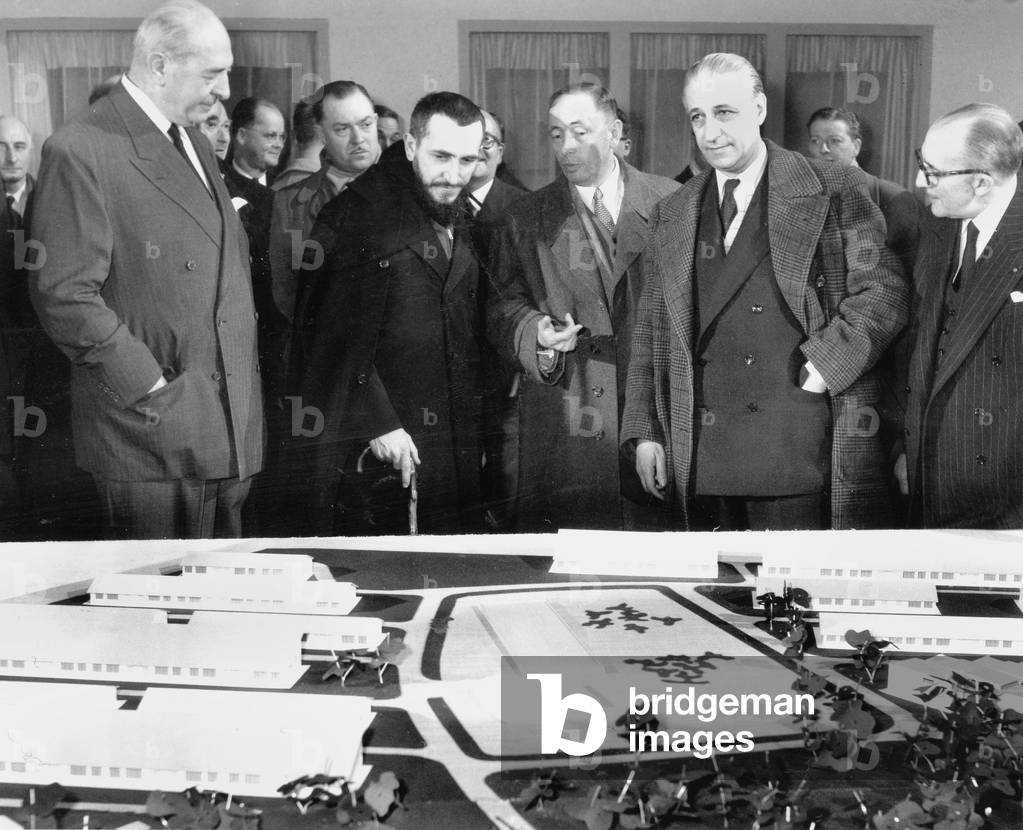 The Abbe Pierre at The Exhibition To Help The Homeless With The Architects Spofry and Dufau in Front of A Scale Model The February 19, 1954, Paris (b/w photo)