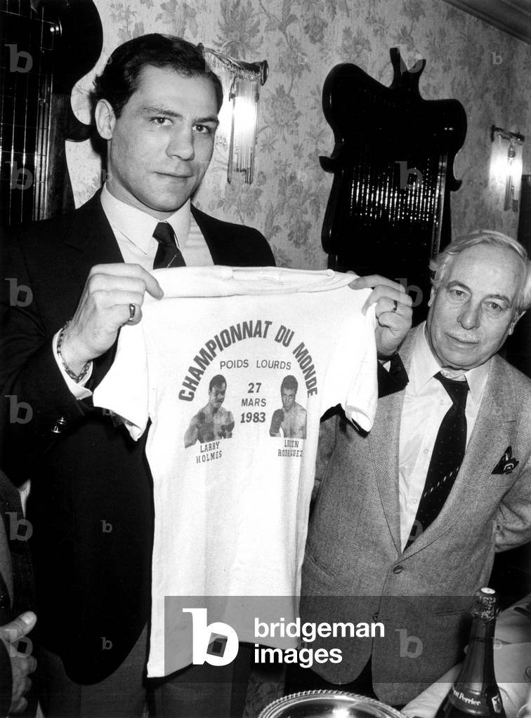 Boxer Lucien Rodriguez Presneting The Tshirt Made For his Admirers in Presence of his Manager Jose Jover, Paris, March 18, 1983 (b/w photo)