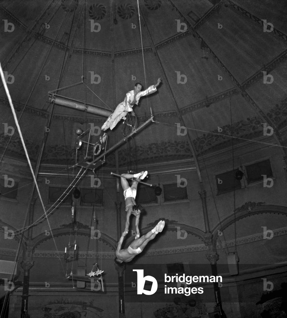 New Show At Circus Medrano Here An Aerien Numero Realised By The Marconis An Acrobat Cyclist Fighter Jongle By Pedaling Over His Partners Who Perform Different Figures At The Trapeze On September 2, 1955 Neg: A11902Bis (b/w photo)