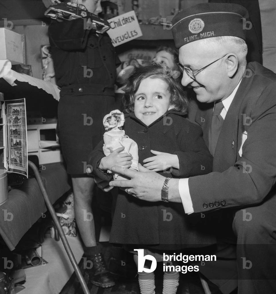 The American Legion is giving European children toys who suffred from war, Paris, March 22, 1951 : here Mich Flynt, member of the American Legion, giving a doll to a French girl (b/w photo)