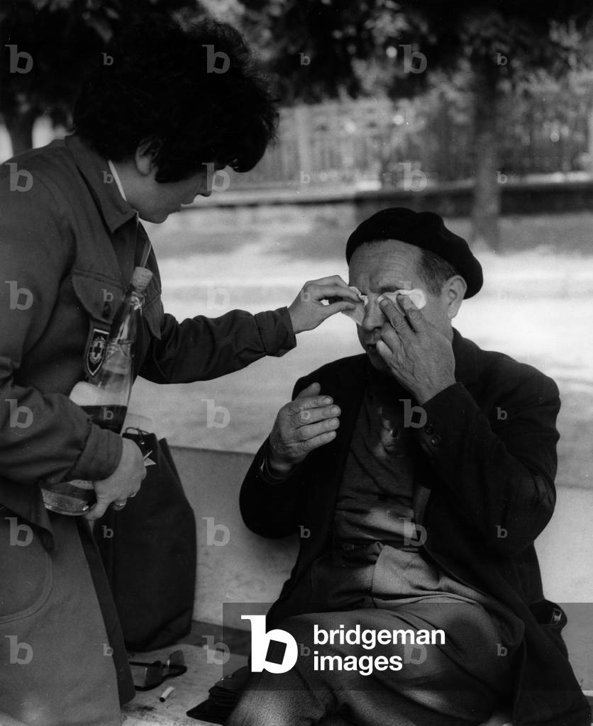 May 68 : A Woman of Red Cross Treating A Wounded Demonstrator in Flins, France, June 7, 1968 (Evacuation of Renault Car Factory) (b/w photo)