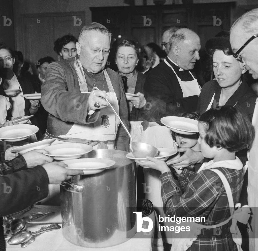 Monseigneur Maurice Feltin, Archbishop of Paris, serving the soup to seniors, at the Little Sisters of the Poor, Paris, March 19, 1951 (b/w photo)