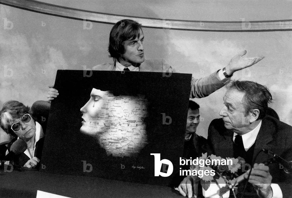Bernard Kouchner of Medecins sans Frontieres, with Yves Montand and Simone Signoret, showing the Poster on Poland designed by Luigi Castiglioni,  December 23, 1981 (b/w photo)