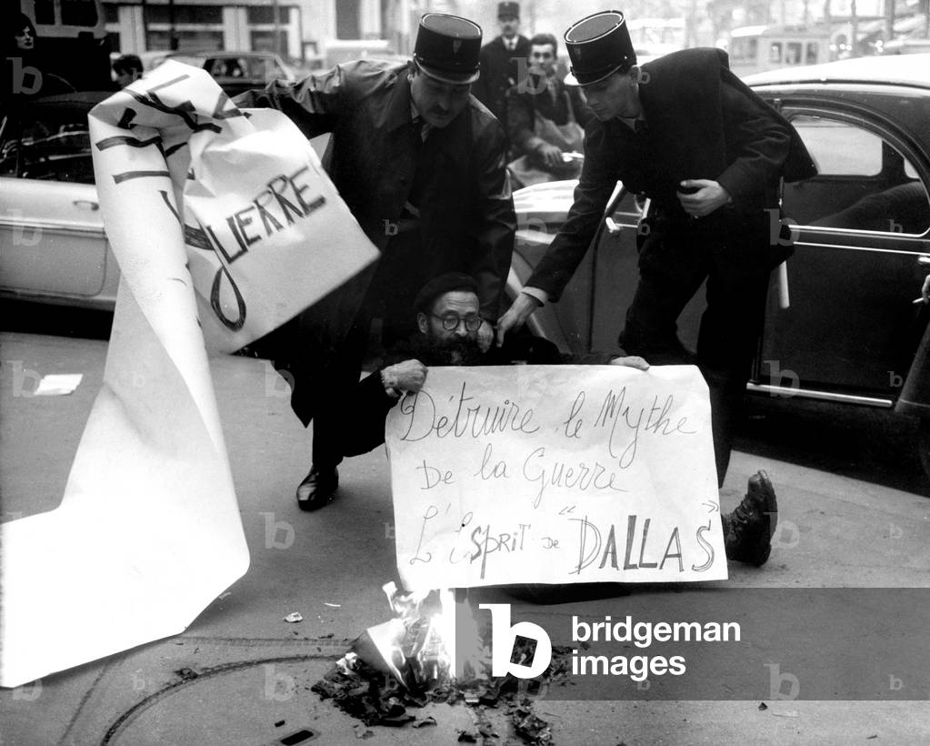 Mouna Aguigui Being Arrested By Policemen While He Was Demonstrating Against War Game Toys, here Holding his Banner With Slogan 
