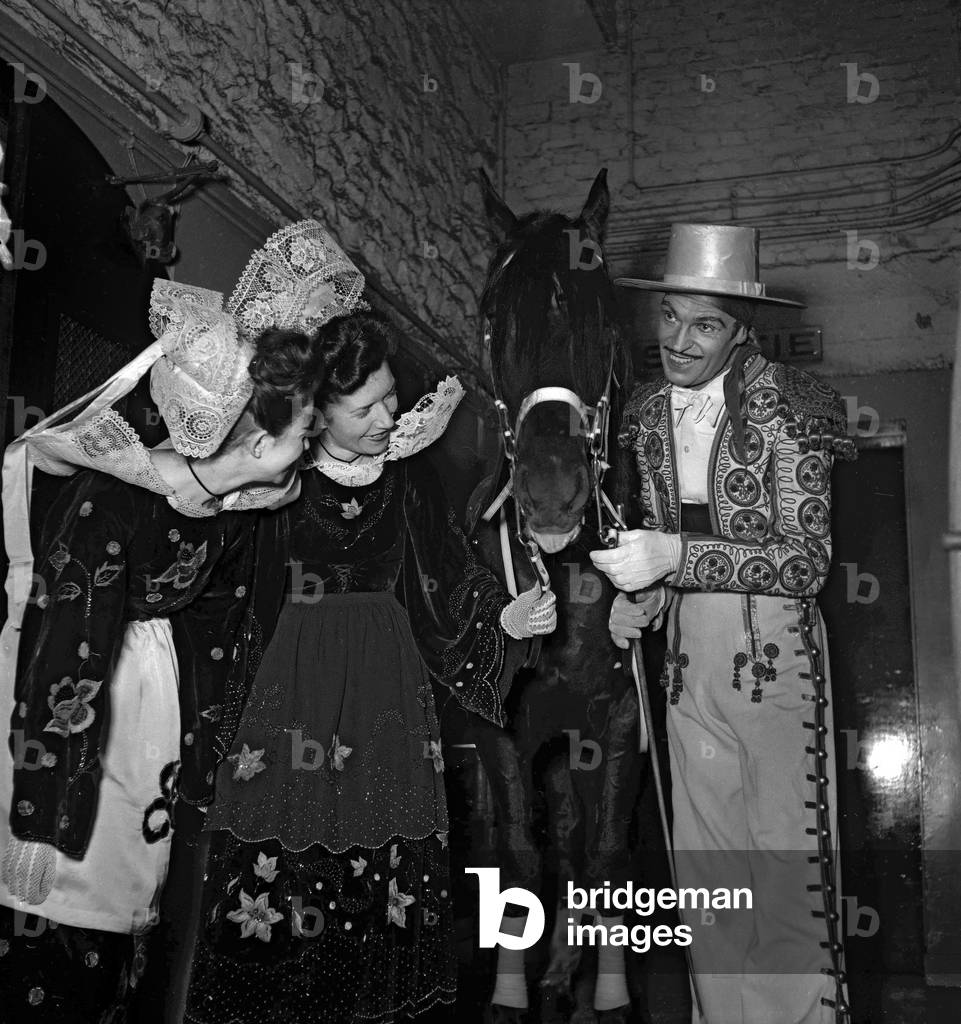 Dance gala, Palais de Chaillot, Paris, June 17, 1949 : Jose Mauser, Spanish dancer, showing his horse to 2 Breton women (b/w photo)