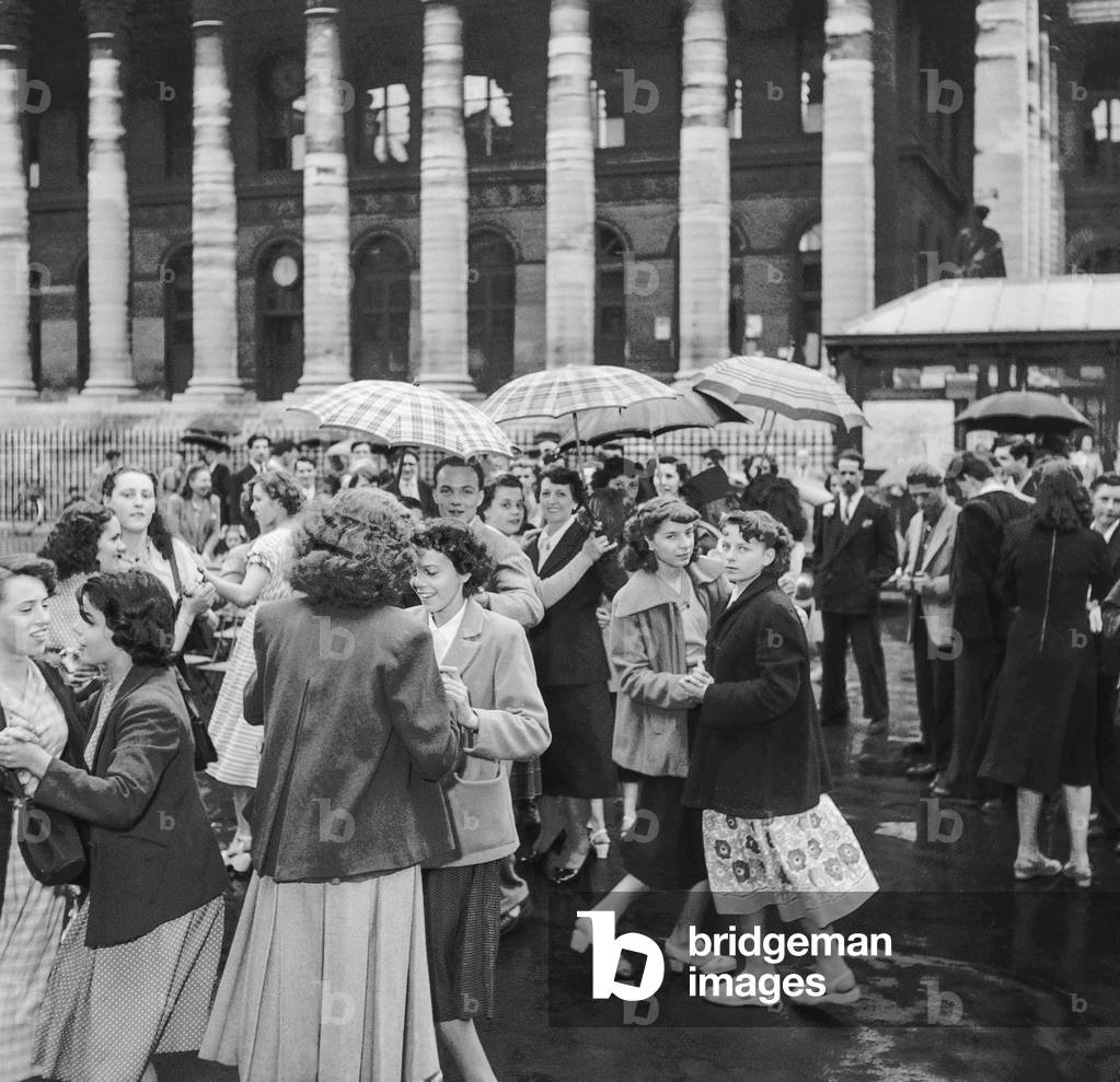 Ball given for the Bastille Day in Paris on July 14, 1950 : outside the Palais Brongniart, people dancing under rain (b/w photo)