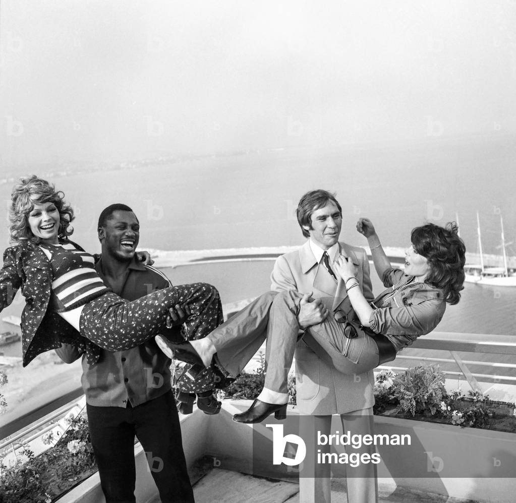 Boxer Joe Frazier carrying Pascale Petit and Jean Claude Bouttier carrying Dani (Daniele Graule) in Antibes, France, June 25, 1971 (b/w photo)