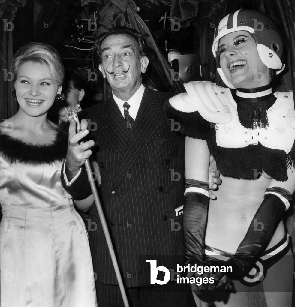 Salvador Dali, Between Miss France 1964 (Jacqueline Giraud) and An Helmeted Stripper of Touchdown Girls, Is Celebrating The 10Th Anniversary of Crazy Horse Saloon on December 9, 1964 (b/w photo)