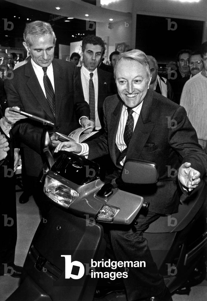 Georges Sarre Trying A Scooter Peugeot Under The Look By Paul Quiles At The Motorcycle Show At The Porte Deversailles November 28, 1991 - (b/w photo)