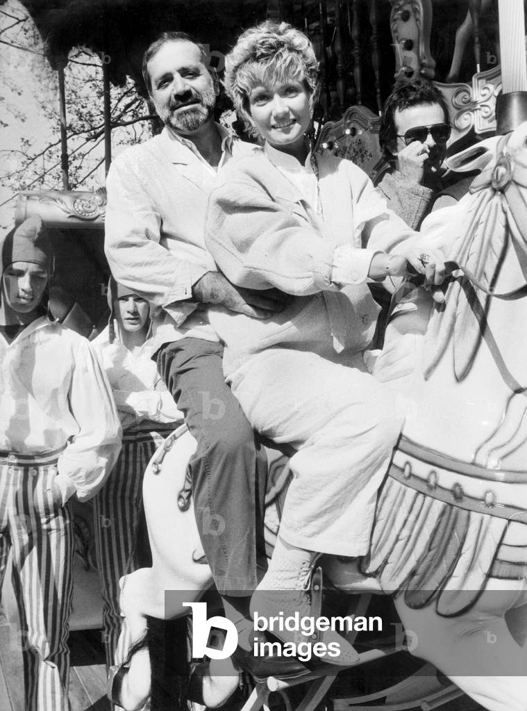 Jean Yanne With Fiancee Actress Mimi Coutelier Riding Merry-Go-Round Horse in Roundabout at Fun Fair in Reuilly April 25, 1985 (b/w photo)