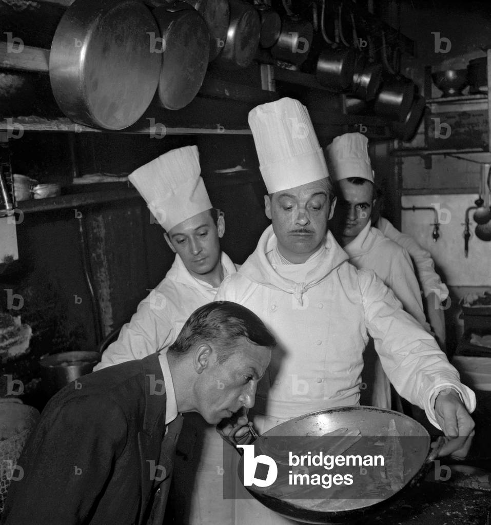 Belgian actor Fernand Gravey preparing meal at restaurant 