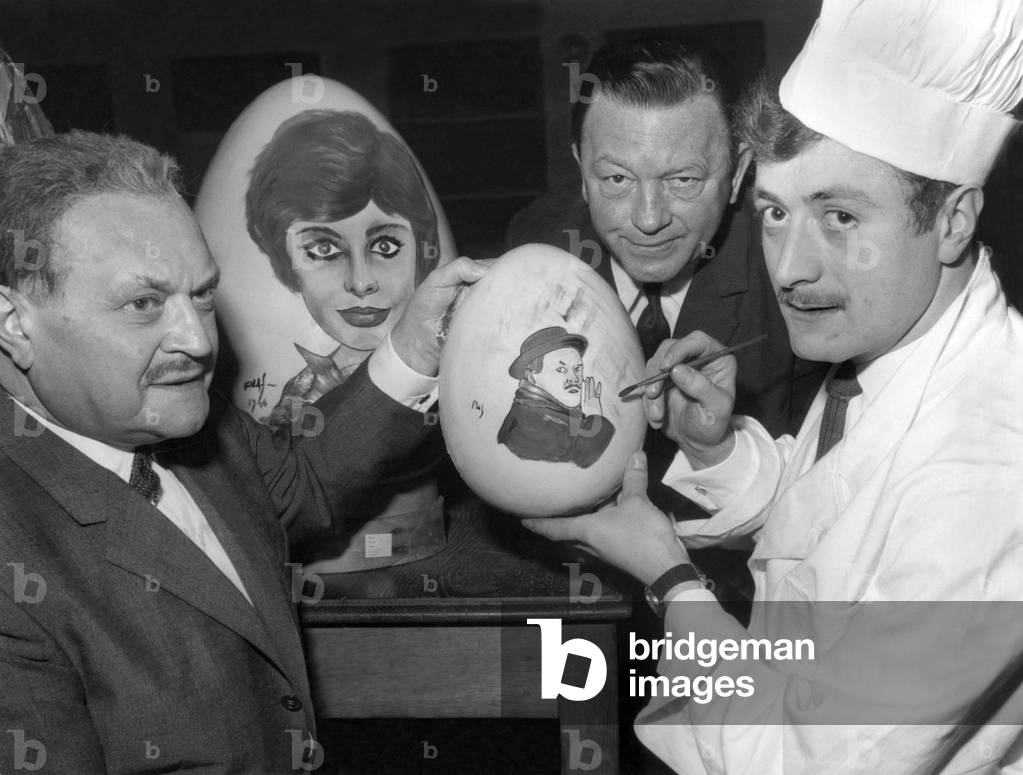 French Actor Raymond Souplex (L) Under The Eye of Jean Daurand and in Front of 2 Big Eggs : One With The Portrait of Sophialoren and the Other With Portrait of Raymond Souplex on April 5, 1966 (b/w photo)
