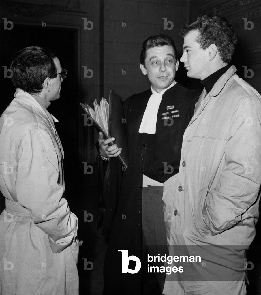 Claude Figus Secretary of Edith Piaf, Here On the Right, (24 Years), Author of a Sacrilege Betting Appeared in front of the 16th Correctional Chamber Where He Was charged with “Violation of Sepulture” (On the Night of December 24 At 2 am, Figus had made the bet to cook two eggs on the dish above the flame of the Unknown Soldier, while He was doing his “Kitchen” He Was Apprehende By Agents After A Breve Pursuit), Here In The Corridors Of The Palace Of Justice On January 23, 1959 (b/w photo)