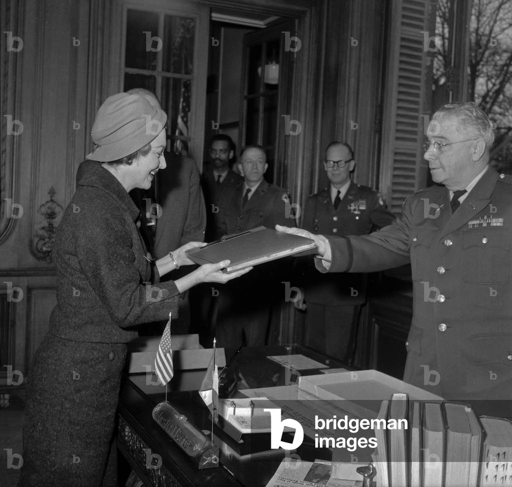 US Colonel Chester Barton offering British-American actress Olivia de Havilland a press article and photo album of the visits and shows she gave for the G.I.'s during the war, in US Army Paris headquarters, on February 26, 1958