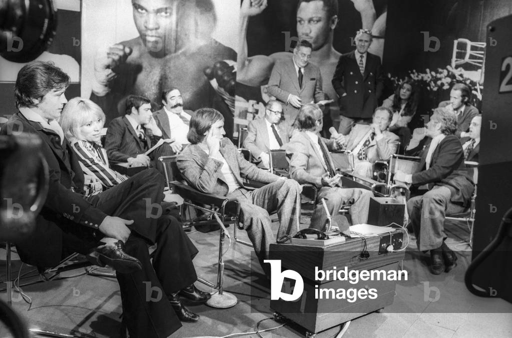 Alain Delon and Mireille Darc looking at television the boxing championship (fight between CassiusClay and JoeFrazier), 1974 (b/w photo)