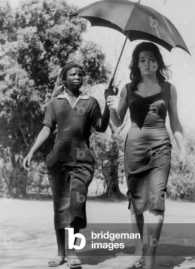 Juliette Greco sheltered of the sun by a young girl during Sky roots film set at Fort Archamsault, 1958 (photo)
