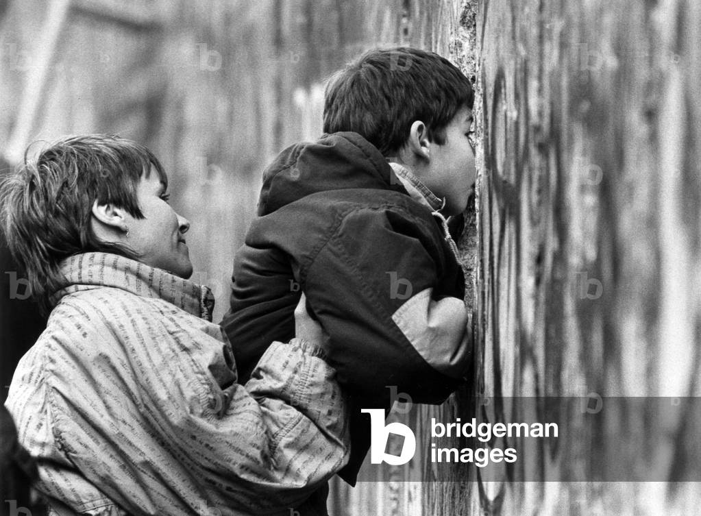A mother helps her son to peep to the East from a hole made in the Berlin wall, 11th November, 1989 (b/w photo)