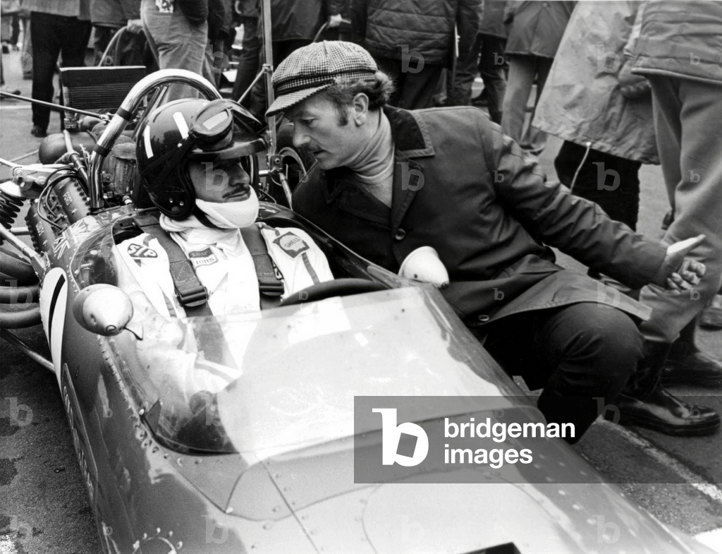 Colin Chapman Designer of The Lotus Cars Chats With his N° 1 Driver Graham Hill Who Won 100 Bottles of Champagne For Setting Up The Fastest Time in Practice As They Wait For The Start of The Race of Champions March 16, 1969 (b/w photo)