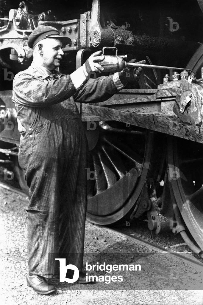 A mechanic oiling wheels of a train, 1940's (b/w photo)