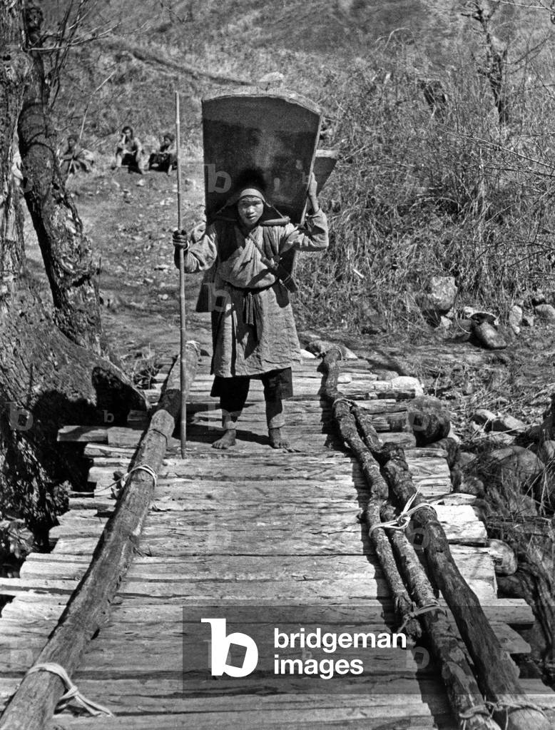 Chinese Lisu people crossing a wooden bridge under construction bringing the boards back one to a 1946-48