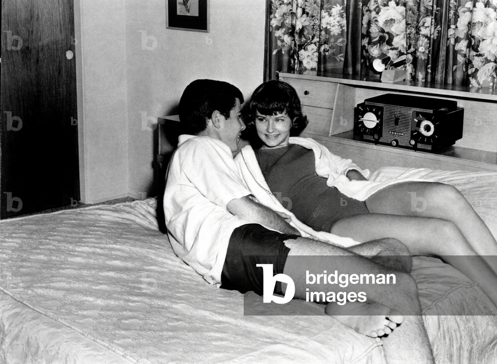 Couple on a bed listenening radio on a Zenith radio set c. 1950