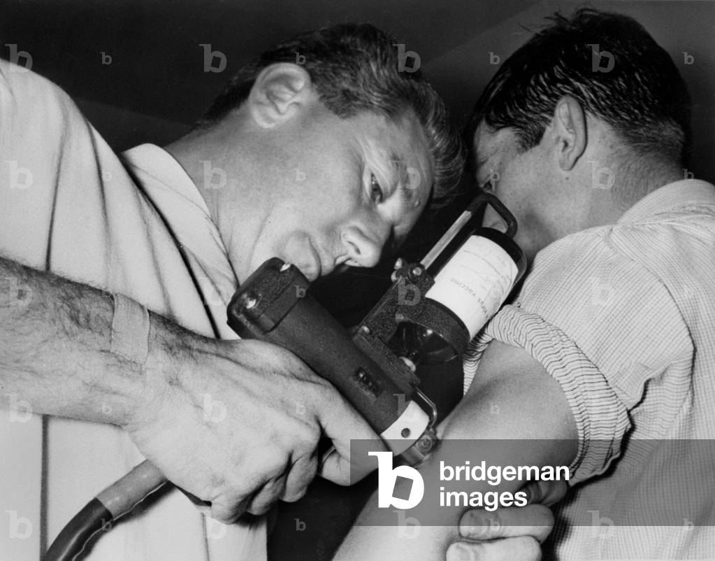 doctor vaccinating football player Clayton against the flu with compressed air gun October 26, 1962