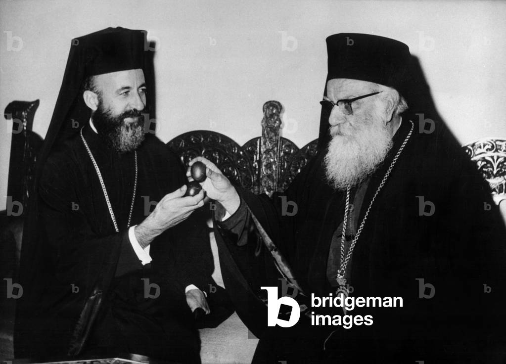 Monsignor Makarios (left) after his captivity in the Seychelles Islands and his return to Athene engaging in the traditional custom of the “clash” of the Easter egg with the Primate of Greece Monsignor Dorotheos (right) on April 26, 1957