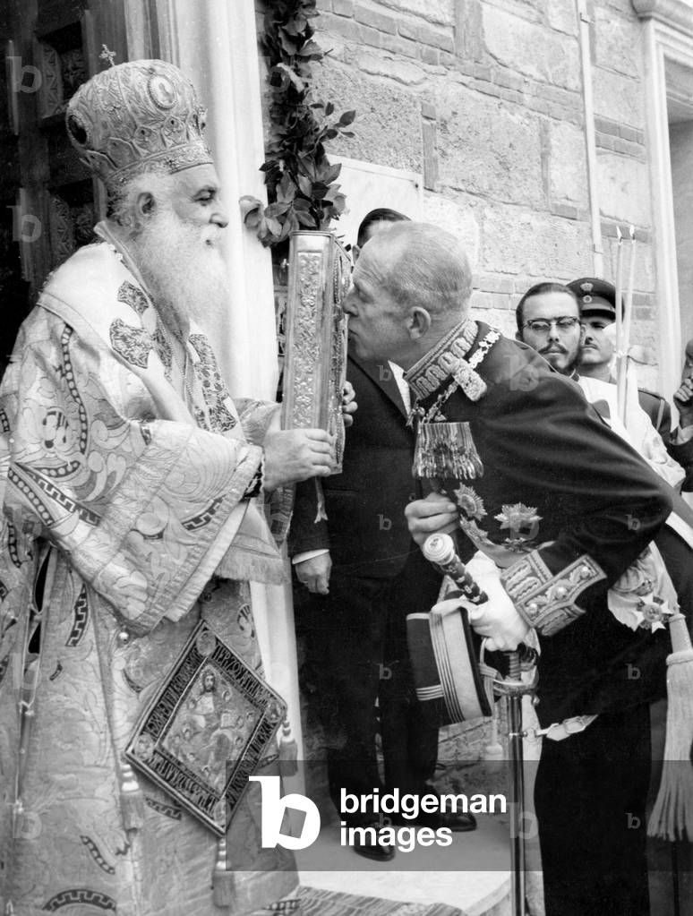 King Paul 1st of Greece kissing the gospel held by archbishop of Salonika during the celebration of 20th anniversary of the Greek refusal to submit to the Italian ultimatum in 1940 , November 11, 1960
