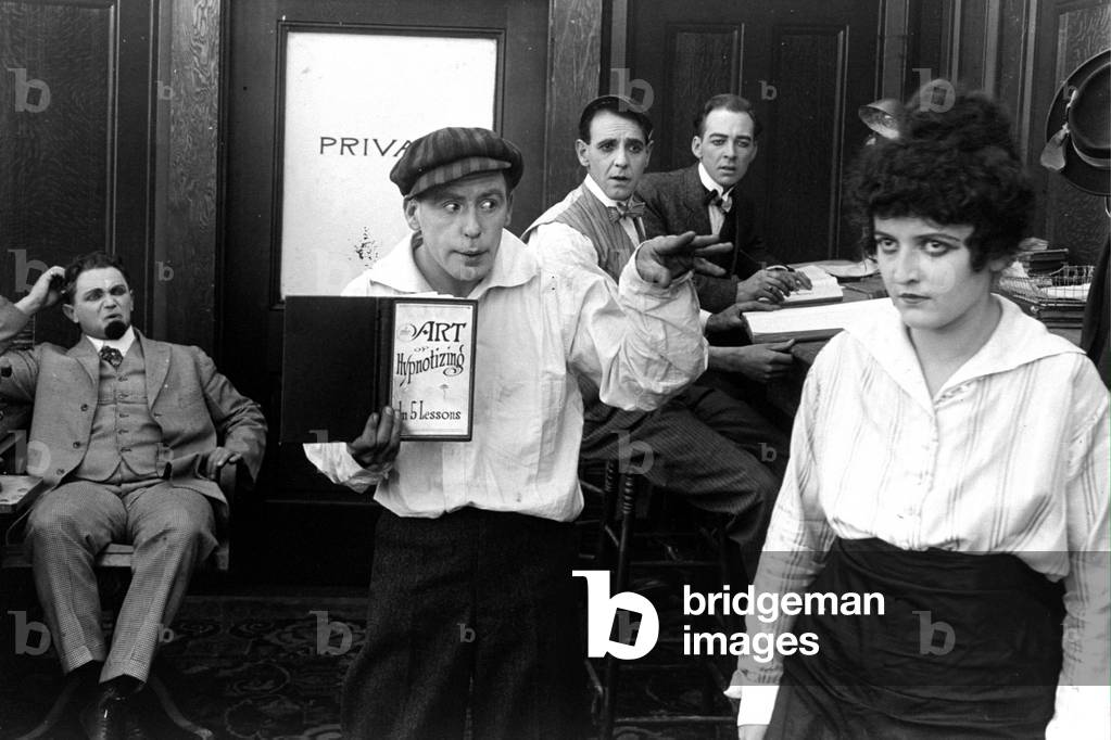 Man hypnotizing a woman in an office under look of his surprised colleagues, 20's