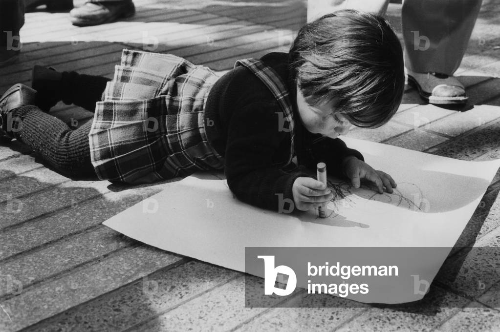 A little girl is drawing on a sheet of paper on the ground during the day of popular expression in Palma de Majorque on April 18, 1979