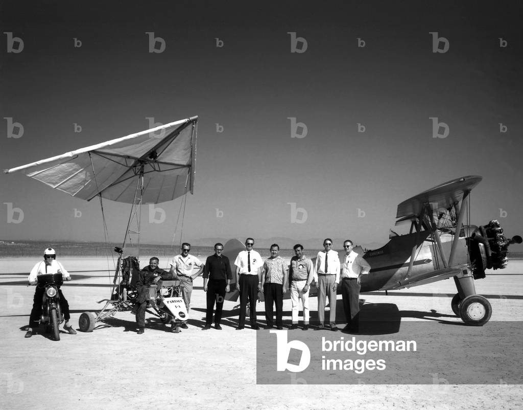Prototype d un Delta Plane 1962 With the Paresev 1-A and the 450-hp Stearman Sport Biplane as a backdrop the pilot and crew pose for this picture in 1962. Starting at left: On the motorcycle is Walter Whiteside, in the Paresev 1-A is test pilot Milton Thompson, Frank Fedor, Richard Klein, Victor Horton, Tom Kelly, Jr., Fred Harris, owner of the Stearman, John Orahood, and Gary Layton.