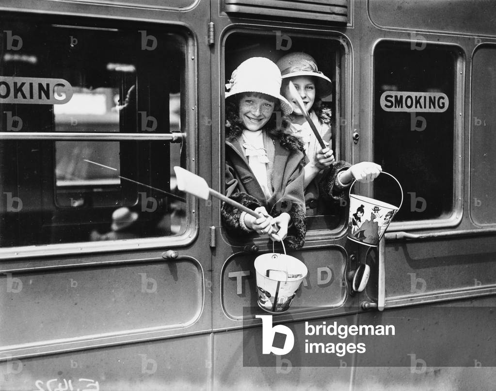 Two young girls (in a third class carriage) leaving London, bound for the seaside. Buckets and
