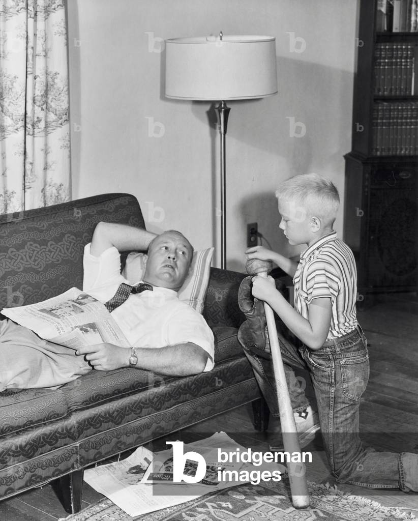 Immagine di Fotografia "Padre sdraiato su un divano con suo figlio inginocchiato accanto a lui", b/w