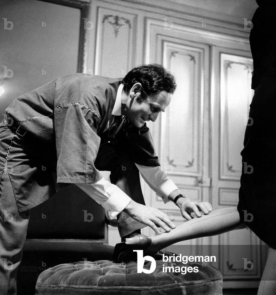 Pierre Cardin untersucht auf dem Bein eines seiner Modelle, wenn ihre Nähstrümpfe gerade ist, 24. Juli 1964 Ne