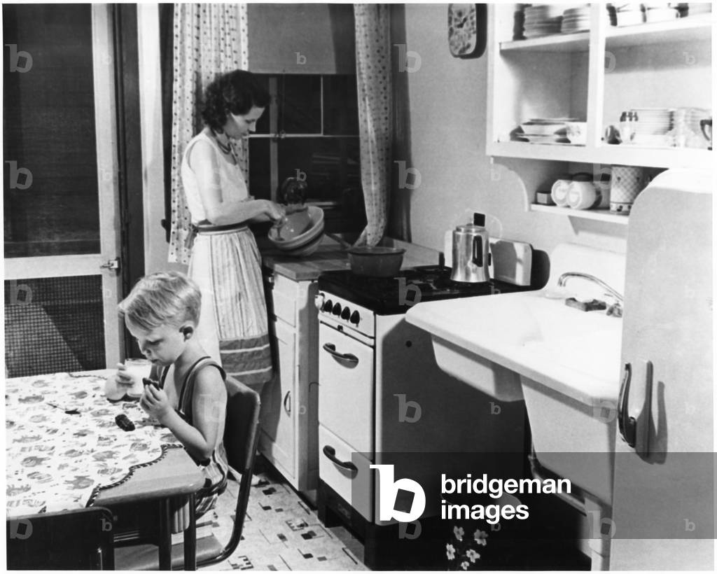 "donna cucina in cucina con giovane ragazzo mangiare biscotti con latte" 1955, b/w